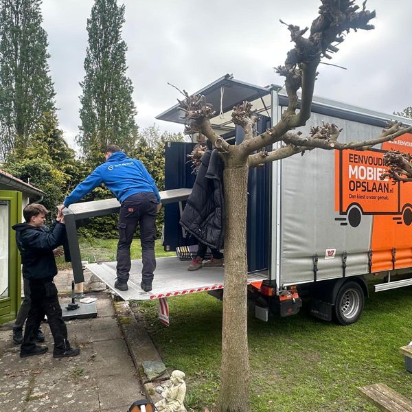Mobiele opslagcontainer eenmalig inladen voor eigen deur – verhuishulp inbegrepen Twee medewerkers laden meubels in mobiele opslagcontainer via laadklep voor woning – Eenvoudig Mobiel Opslaan